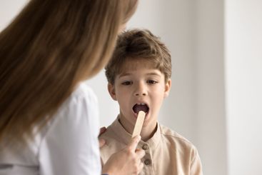 Female doctor look at little boy throat using medical...