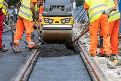 Steamroller workers construct asphalt road and railroad...