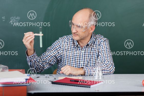 Professor Looking At Test Tube While Wearing Protective...