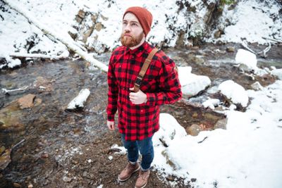 Pensive bearded young man standing near mountain river in...