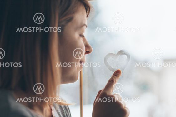 Young woman drawing a heart on the window