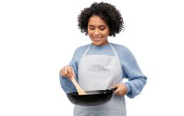 smiling woman in apron cooking food in frying pan