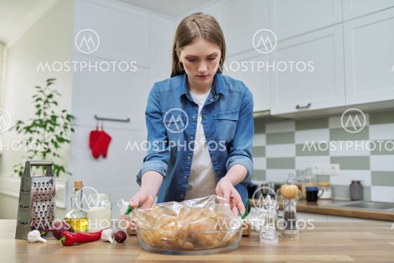 Young woman cooking baked chicken in baking sleeve with...