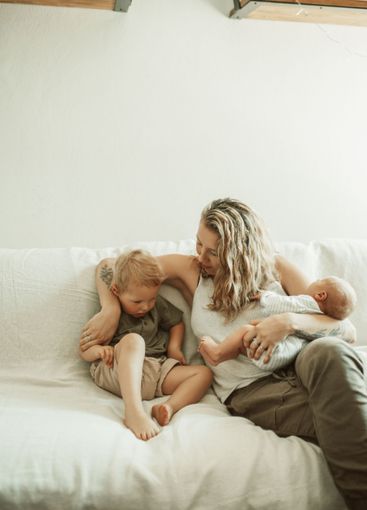 Mom, baby and sibling on sofa in home living room with...