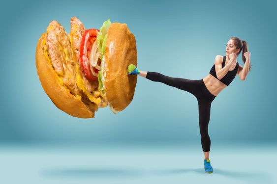 Fit, young, energetic woman boxing hamburger as unhealthy...