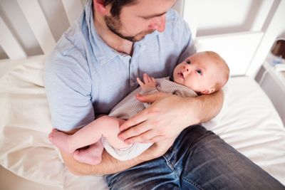 Young father holding his newborn baby son, home bedroom