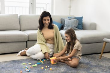 Cute little kid girl playing with mother seated on floor