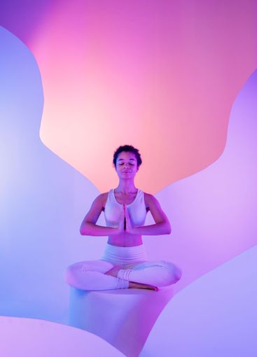 Young African woman in fitness suit sits cross-legged in...
