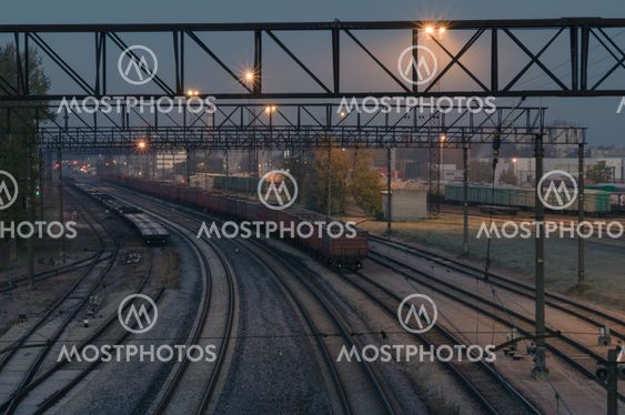Illuminated cargo train station by night. Curve platform with containers