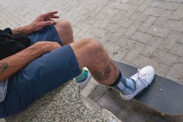 Man, skateboard and legs to relax in city, smoking...