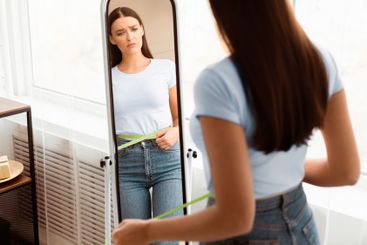Sad Woman Measuring Waist After Weight Gain Standing At...