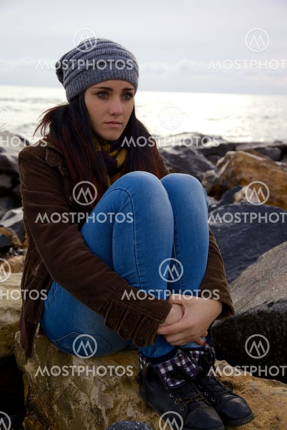 Cute young woman thinking feeling emotion on rocks in front of the sea
