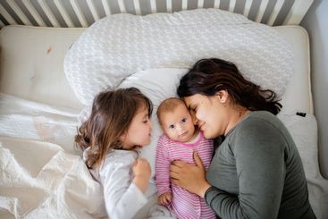 Mother Resting on a Bed with Her Two Happy Young...