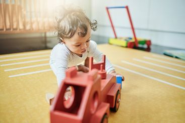 Baby, boy and wooden car toys on floor in nursery,...