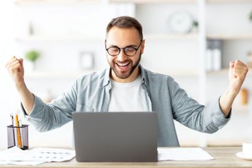Young Caucasian guy gesturing YES in front of laptop,...