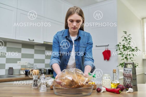 Young woman cooking baked chicken in baking sleeve with...