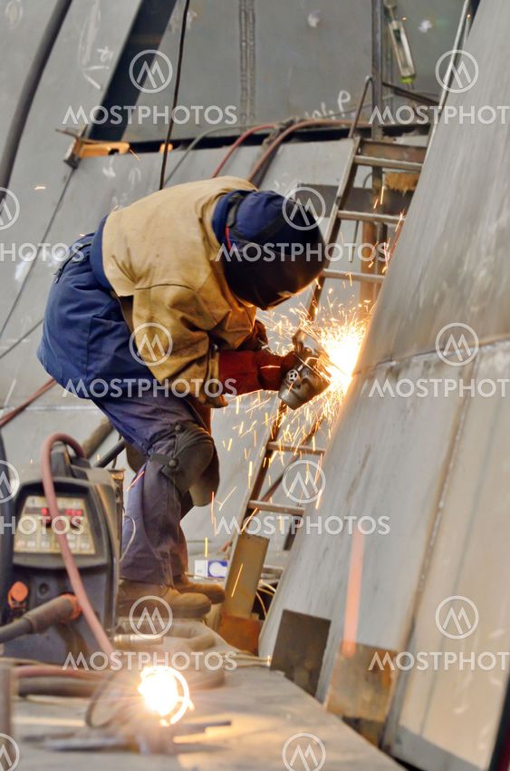 worker grinding metal inside of shipyard