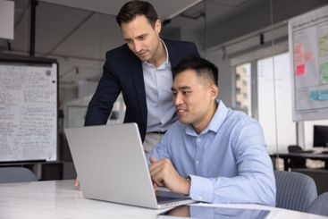 Confident male boss watching Asian manager man working...