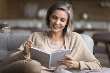 Smiling 50s female spend evening at home read book