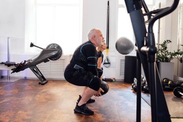 Elderly man in ems suit is training with personal...