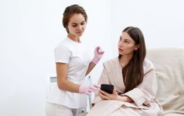 Young female cosmetologist and patient engage in beauty...