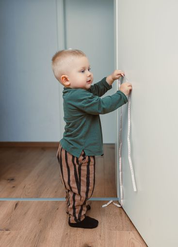 A joyful toddler is measuring their height using a tape...