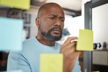 Office, black man and writing with sticky note for...