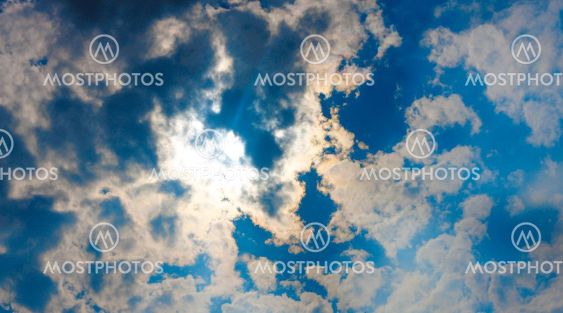 Stormy white clouds on blue sky and sun behind clouds