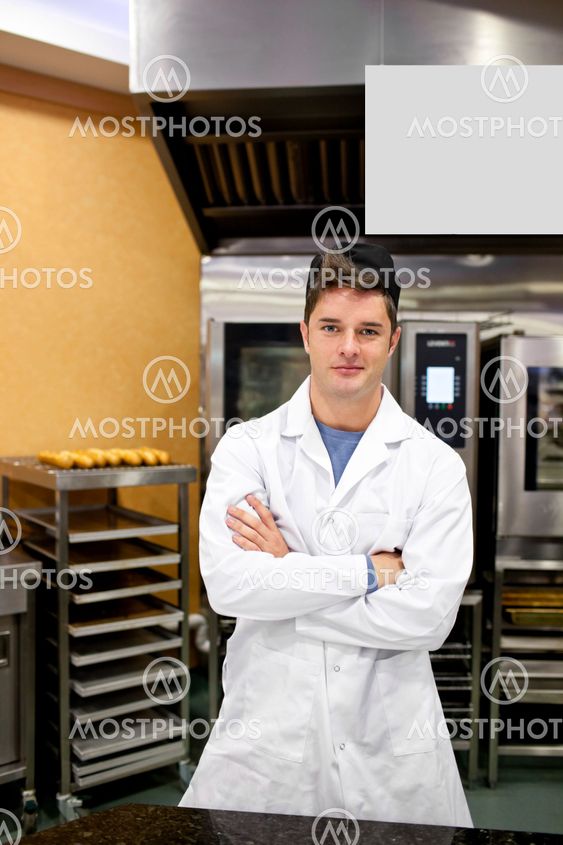 Proud baker standing in his kitchen bending his arms waiting for his baguettes