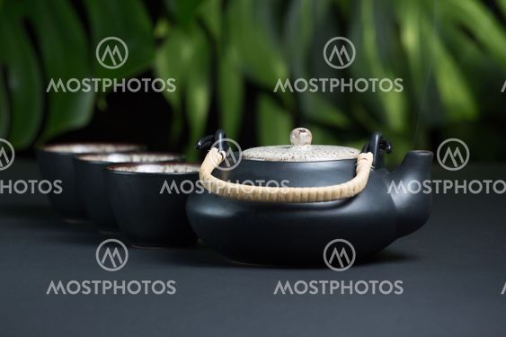 Black ceramic teapot with cups and steam