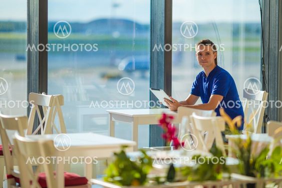 Young man working with laptop at airport cafe w