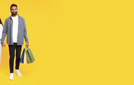 Happy Arab Couple Walking With Shopping Bags On Yellow...