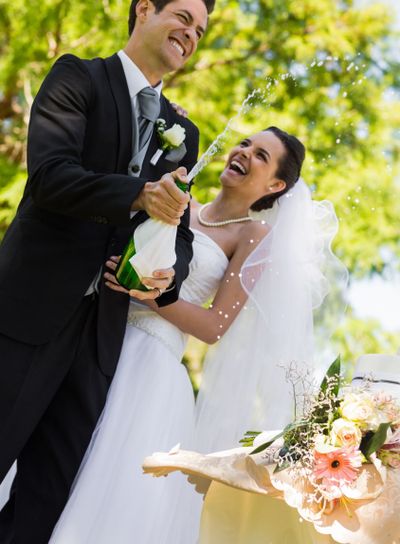 Newlywed couple with groom opening champagne bottle at park
