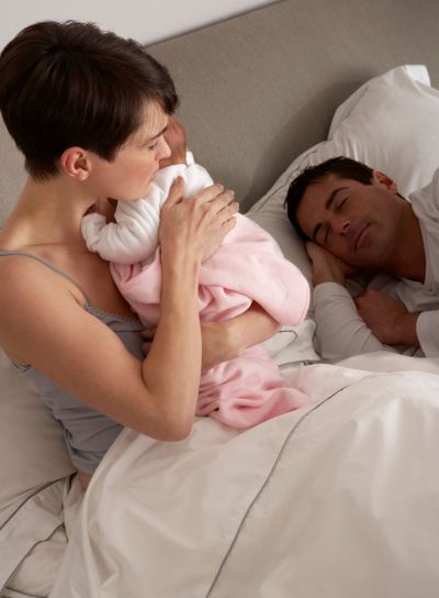 Mother Cuddling Newborn Baby In Bed At Home