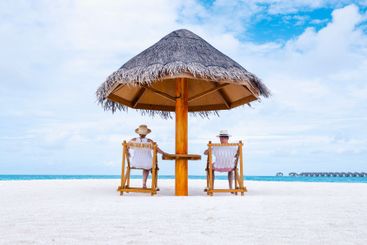 A young married couple is sitting under a straw umbrella...