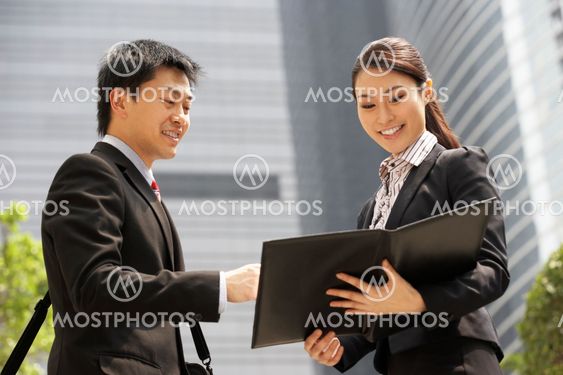 Chinese Businessman And Businesswoman Discussing Document Outside Office