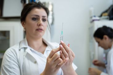A focused nurse in a white lab coat carefully prepares a...