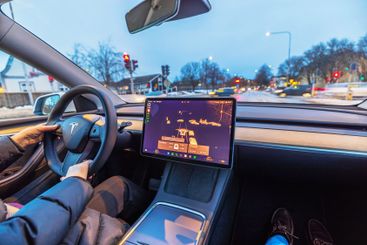 Woman driving Tesla Model Y through city at dusk 
