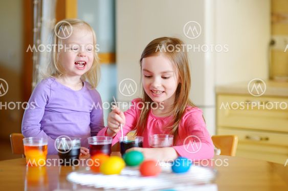 Two little sisters painting colorful Easter eggs
