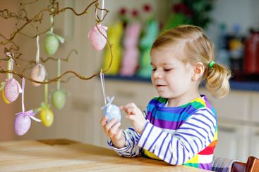 Cute little toddler girl decorating tree bough with...