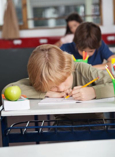 Tired Schoolboy Sleeping At Desk