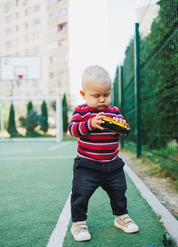 A fair-haired one-year-old boy in jeans and sneakers...