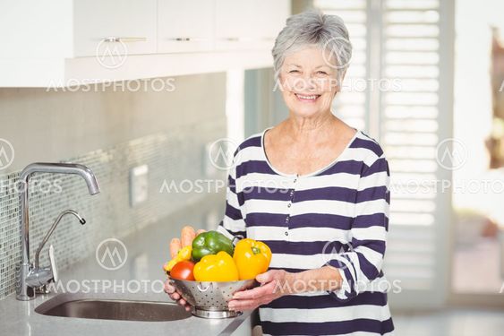 Portrait of senior woman holding colander with vegetables