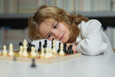 Concentrated child play chess. Kid playing board game....