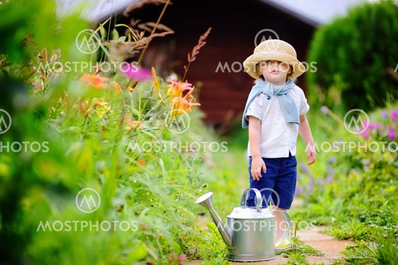 Toddler boy in straw hat watering plants in the garden