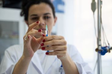 A focused nurse in a white lab coat carefully prepares a...