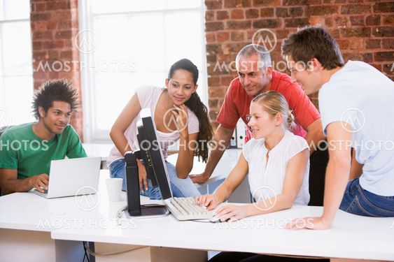 Five businesspeople in office space looking at computer...