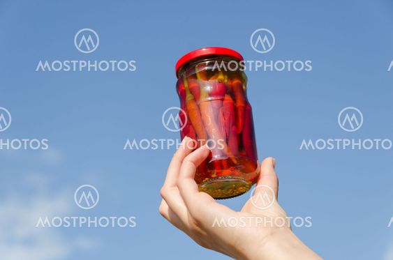 chili pepper jar in hand on blue sky background