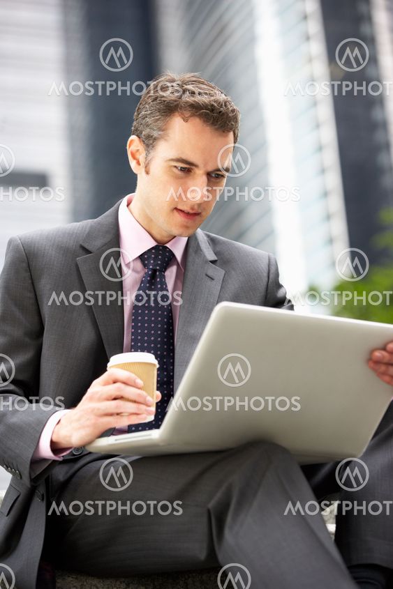 Businessman Working On Laptop Outside Office With Takeaway Coffee