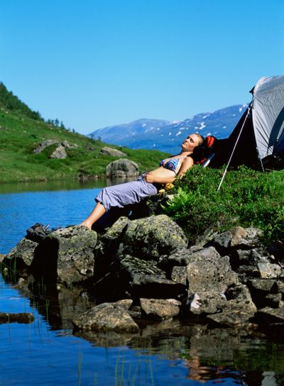 Young woman sunbathing on rocks next to lake